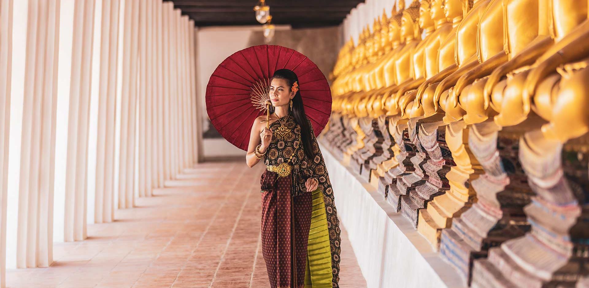 Kvinde I Traditionel Kjole Gaar Ved Buddah Statuer Med Paraply
