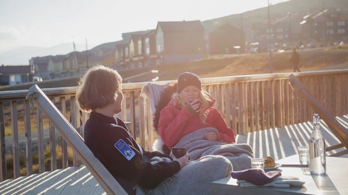 To kvinder nyder solen på terrassen og nyder en kop kaffe