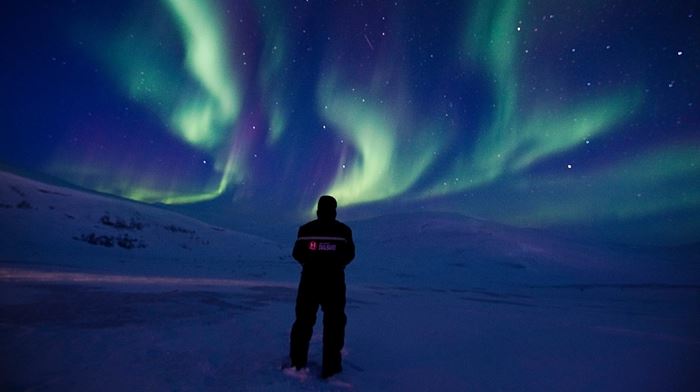 Mand i termotøj beundrer nattenhimlen med nordlys i grønt