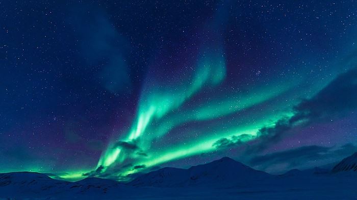 Nordlys i grønne farver danser henover himlen og bjergtoppe