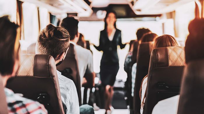 Kvindelig guide står på bus og snakker til passagere