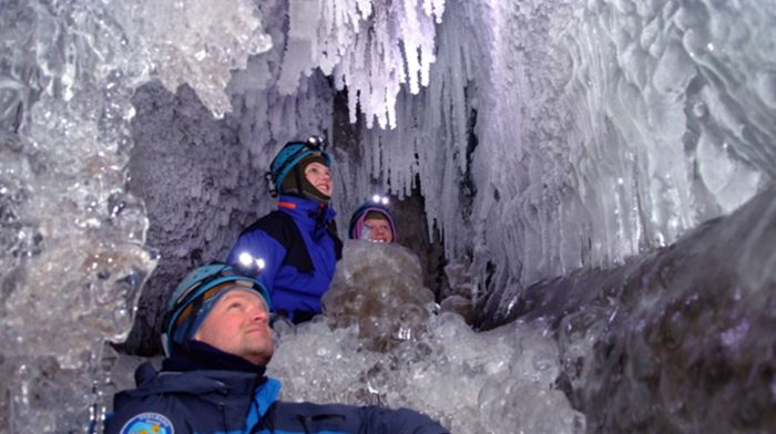 Tre mennesker ser på iskrystaller i isgrotten