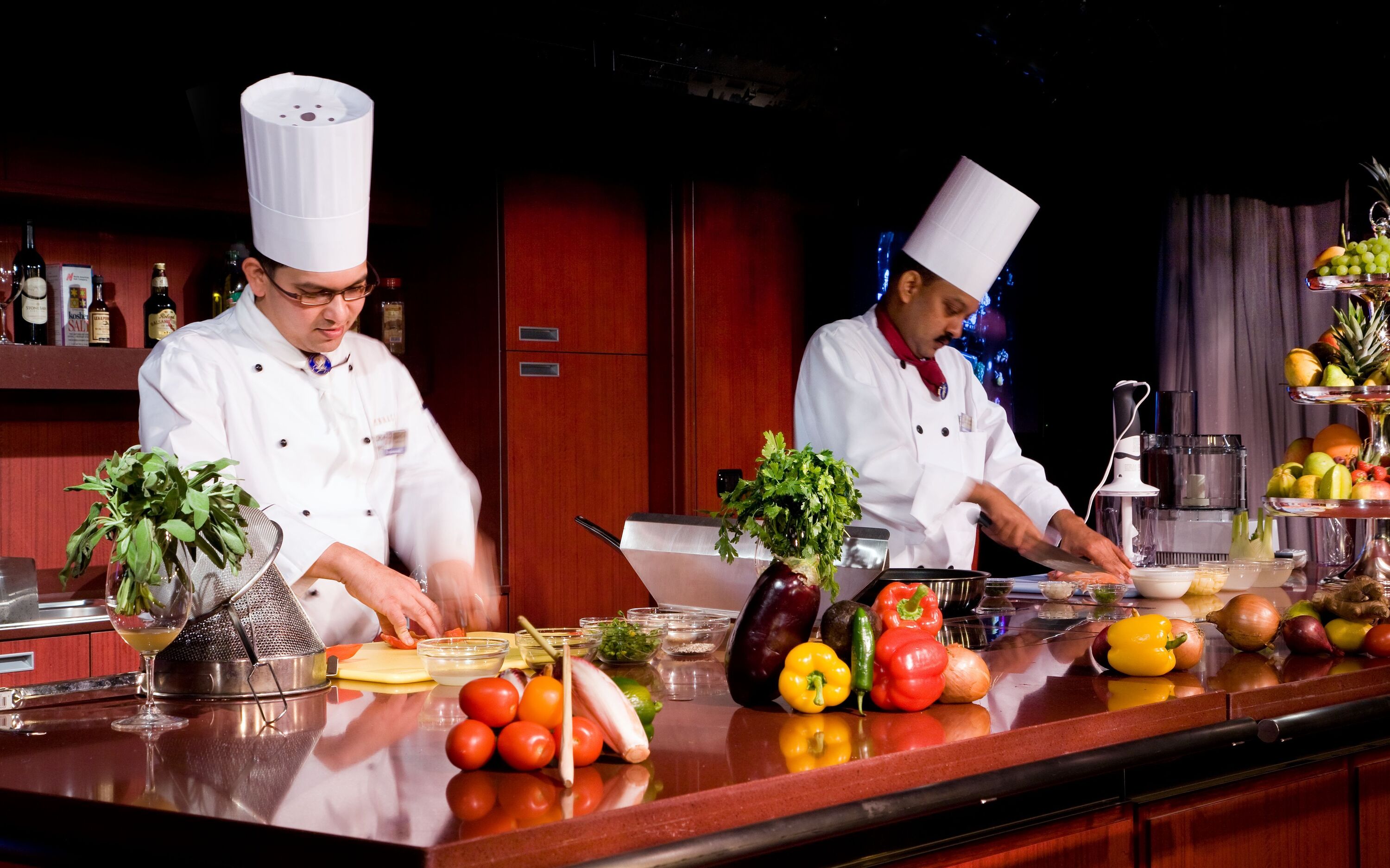 Professionelle kokke demonstrerer madlavning med friske ingredienser i kulinarisk center ombord på Holland America Line