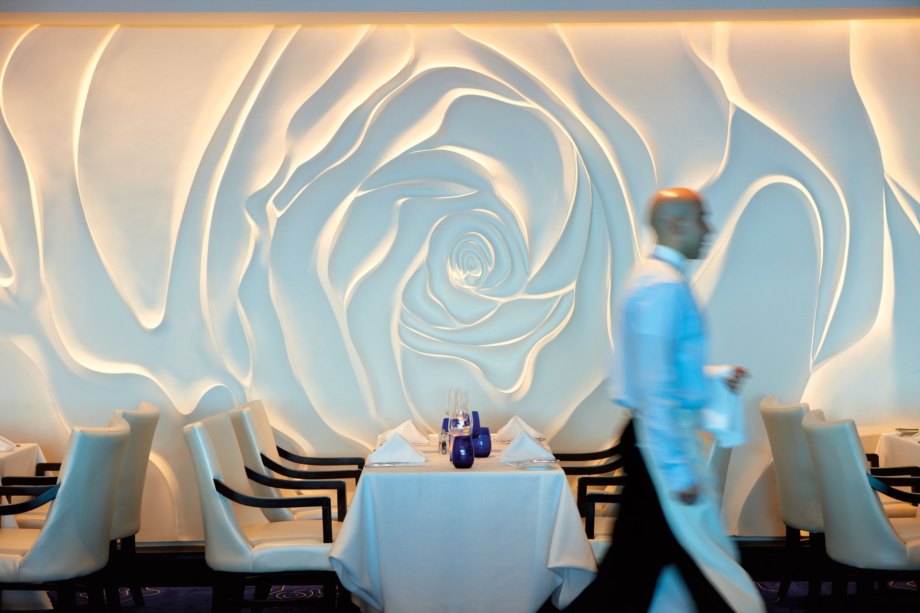 Blu på Celebrity Equinox – Specialrestaurant med skulpturel rosedekoration på bagvæggen og minimalistisk hvid indretning