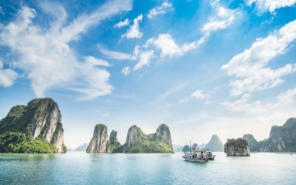 Dramatiske kalkstensøer i Halong Bay Vietnam med traditionel båd sejlende i smaragdgrønt vand