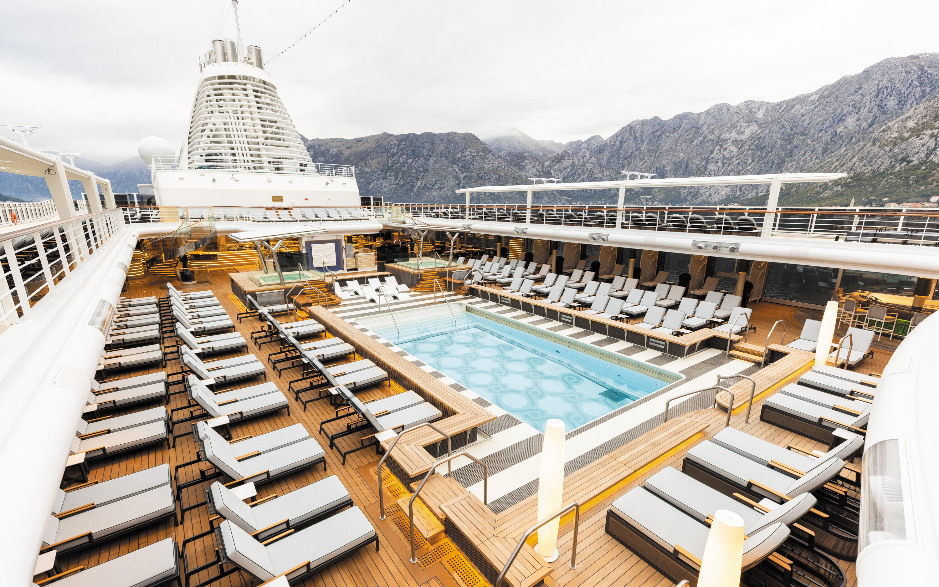 Pooldæk på Regent Seven Seas Voyager med liggestole og bjerglandskab i baggrunden