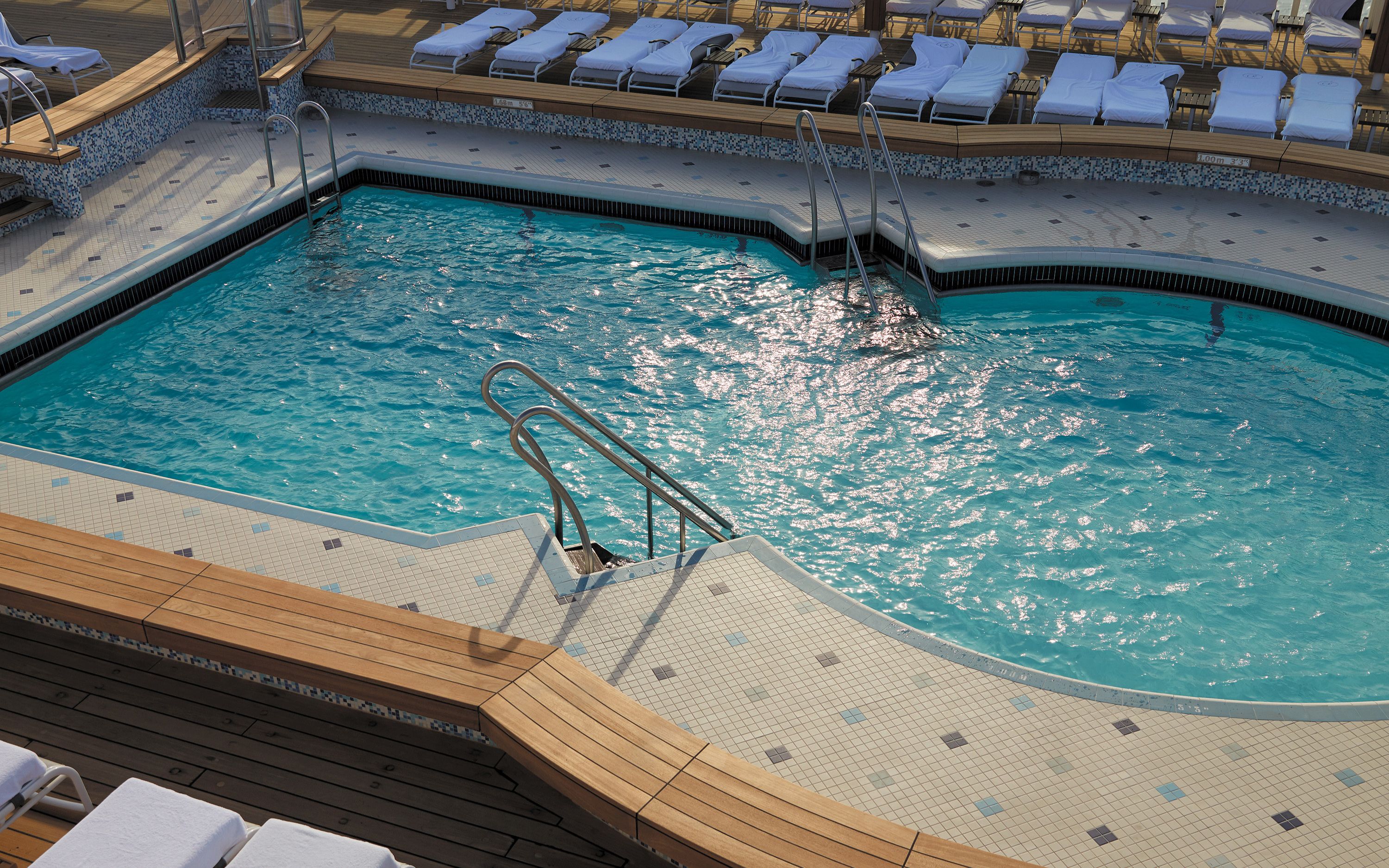 Skibets udendørs pool på Seven Seas Voyager omgivet af solsenge på teakdæk