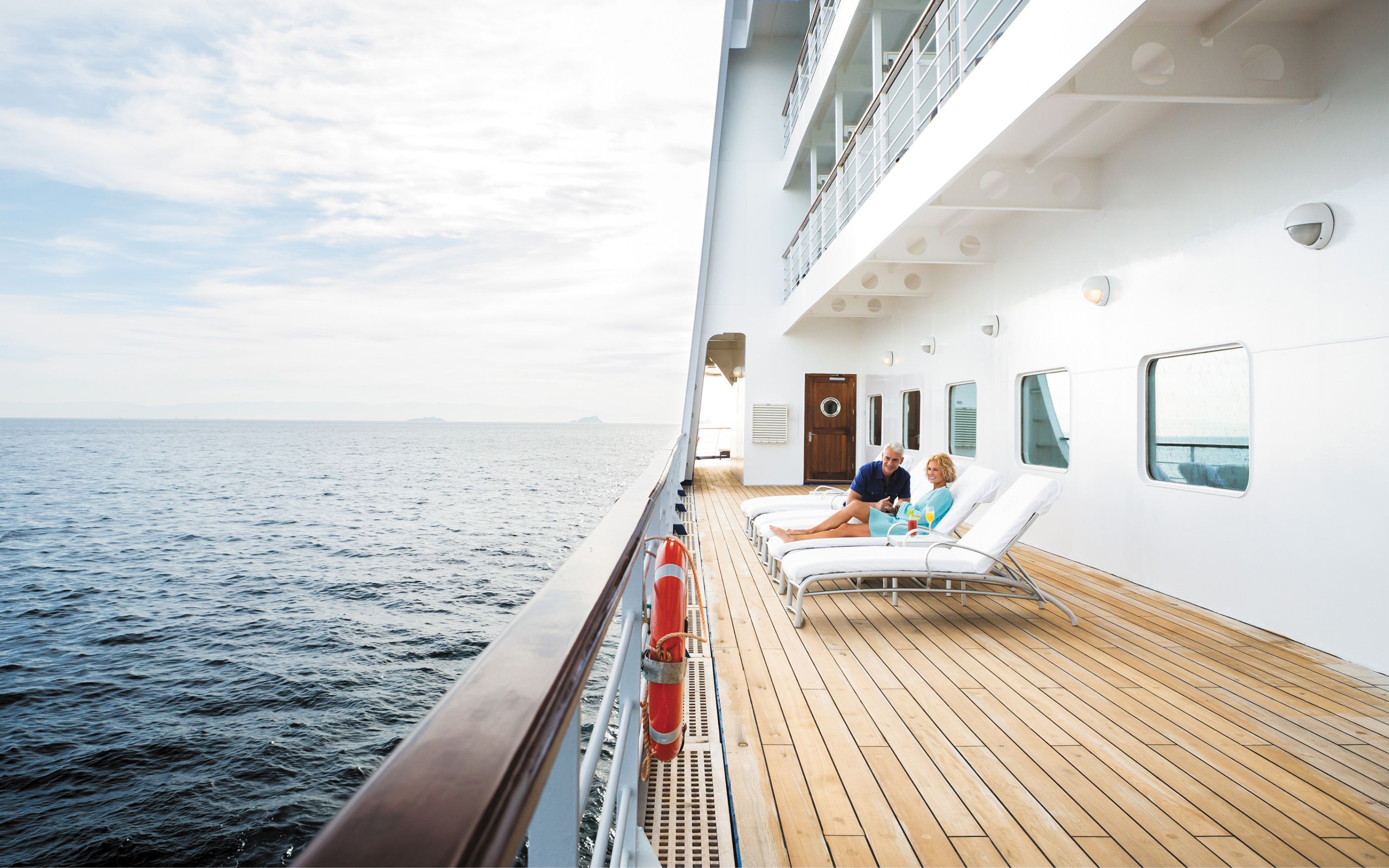 Par slapper af på liggestole på krydstogtskibet Regent Seven Seas Voyager med udsigt til åbent hav