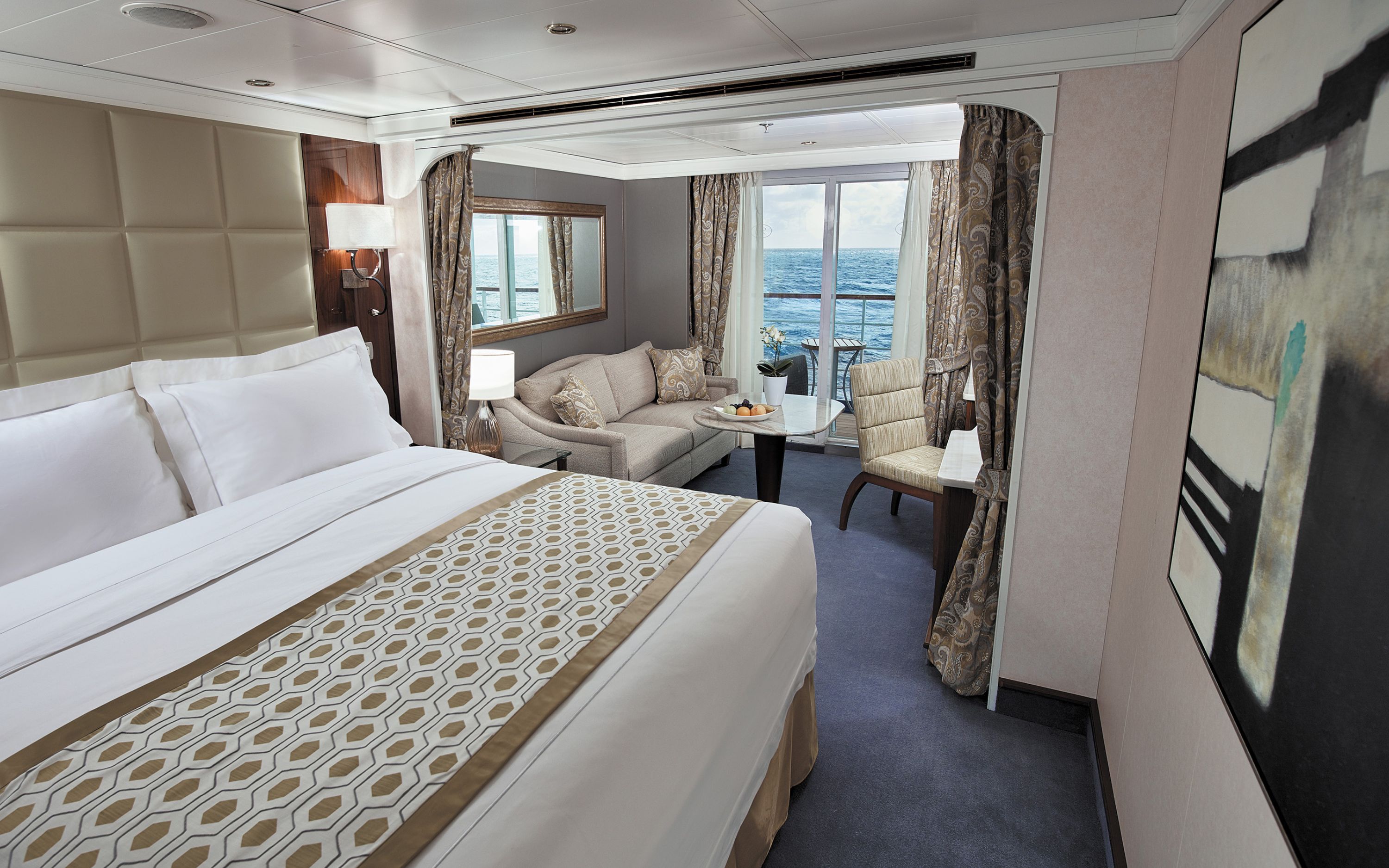 Luksuriøs suite på Seven Seas Voyager med dobbeltseng, sofa og privat balkon med havudsigt