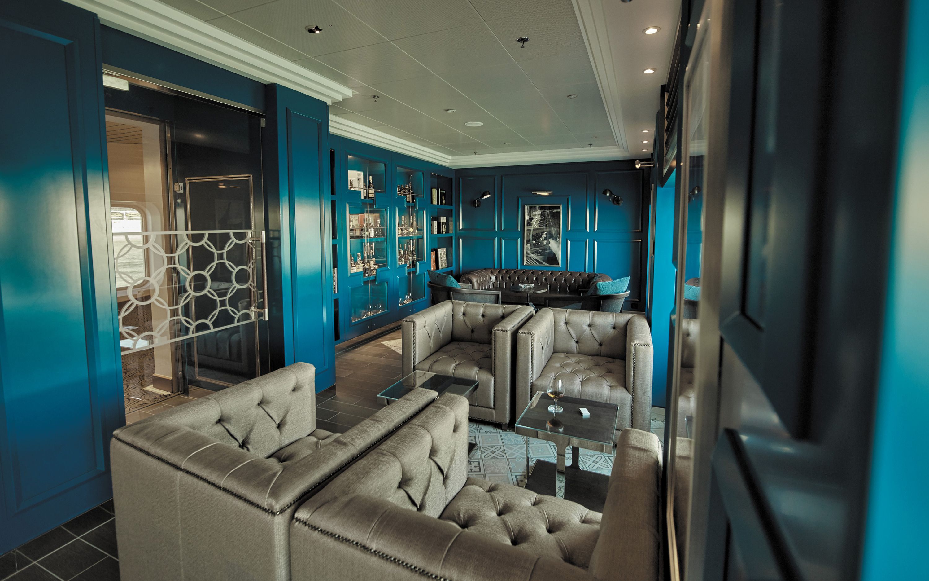 Eksklusiv lounge med blå vægge, lædermøbler og glastable på Seven Seas Voyager